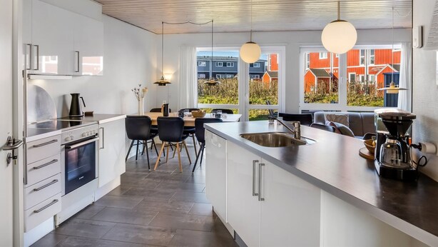 Ett modernt kök med en central köks ö, inbyggda vitvaror och stora fönster som ger utsikt över området.