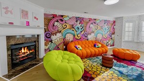 A living room with a fireplace, colorful artwork, and orange bean bag chairs. - Funk-Shui Vibrant Designer Getaway (Atlanta)