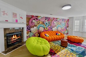 A living room with a fireplace, colorful artwork, and orange bean bag chairs. - Funk-Shui Vibrant Designer Getaway (Atlanta)
