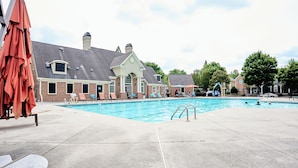 A swimming pool with lounge chairs and umbrellas, a brick building with a gabled roof, and a clear sky. - Funk-Shui Vibrant Designer Getaway (Atlanta)