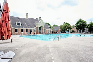 A swimming pool with lounge chairs and umbrellas, a brick building with a gabled roof, and a clear sky. - Funk-Shui Vibrant Designer Getaway (Atlanta)
