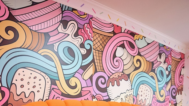 A vibrant orange bean bag chair with colorful toys, set against a wall with a whimsical ice cream-themed mural. - Funk-Shui Vibrant Designer Getaway (Atlanta)