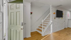 A hallway with a wooden floor, a white door with a keypad lock, a staircase with white railings, and a wall-mounted television. - Funk-Shui Vibrant Designer Getaway (Atlanta)