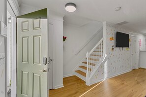 A hallway with a wooden floor, a white door with a keypad lock, a staircase with white railings, and a wall-mounted television. - Funk-Shui Vibrant Designer Getaway (Atlanta)
