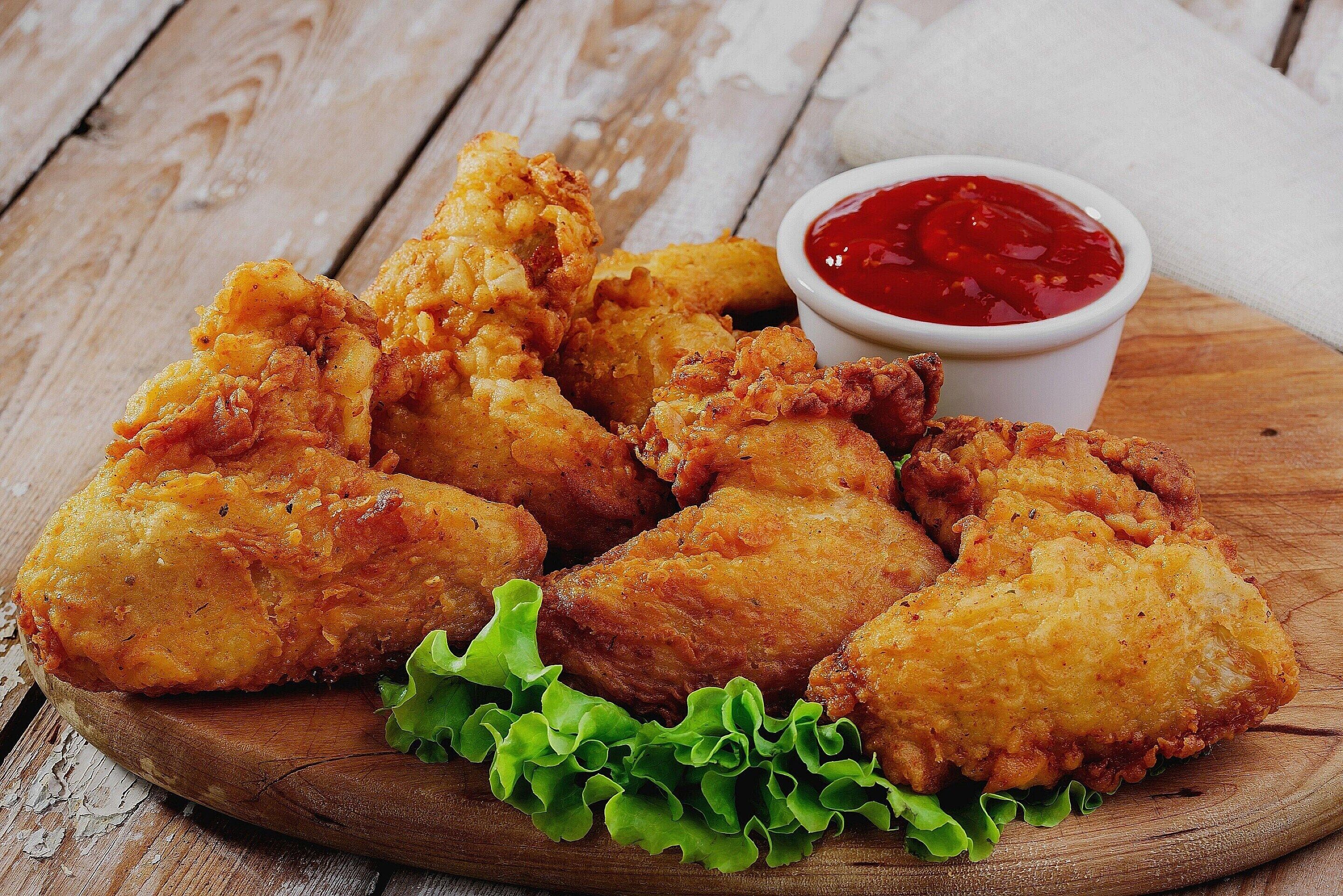 Morceaux de poulet frit disposés sur une planche en bois, accompagnés de laitue et d’un petit bol de sauce rouge.