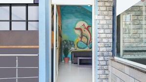 A hallway with a blue wall, a checkered sofa, a potted plant, and a mural. - Super Collection O Chikmangaluru (Chikkamagaluru)