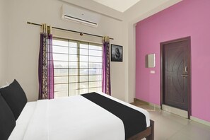 A hotel room with a bed, a window with curtains, a door, and an air conditioning unit.
