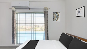 A hotel room with a bed, a window with curtains, a wall-mounted air conditioner, and two framed pictures. - Super Collection O Chikmangaluru (Chikkamagaluru)