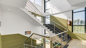 A modern staircase with metal railings, a fire extinguisher mounted on the wall, and a view of the outdoors through large windows. - Super Collection O Chikmangaluru (Chikkamagaluru)