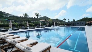 Una piscina con lettini e ombrelloni, circondata da palme e un paesaggio collinare.