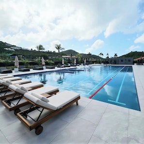 Ein Swimmingpool mit Liegestühlen und Sonnenschirmen, umgeben von Palmen und einer hügeligen Landschaft.