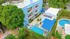 Ein mehrstöckiges Hotel mit Pool auf dem Dach, einem separaten Schwimmbecken und einem üppigen, grünen Garten.