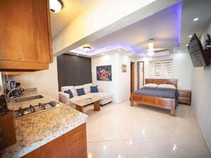 Eine moderne Küche mit integriertem Herd, ein Essbereich mit Tisch und Stühlen, ein Sofa und ein Schlafzimmer mit Bett und Nachttisch.