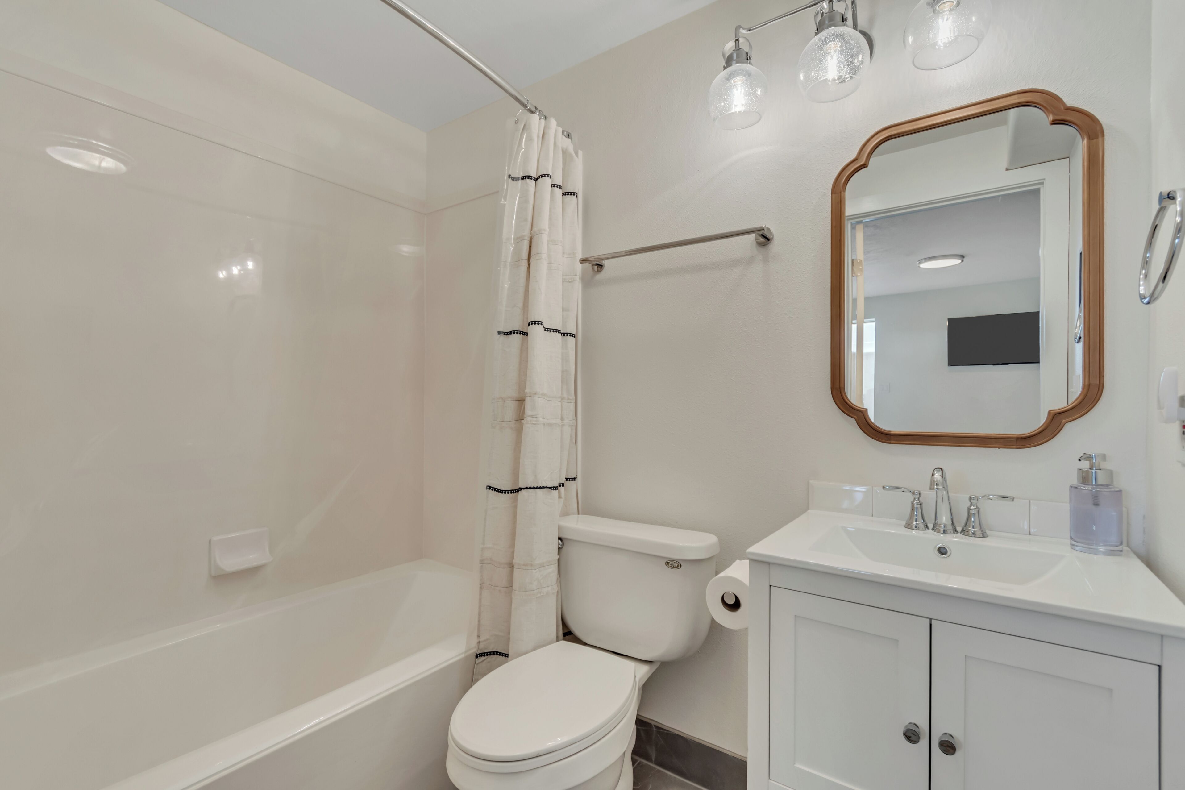 A bathroom with a white toilet, a shower curtain, a bathtub, a sink with a mirror, and a light fixture.