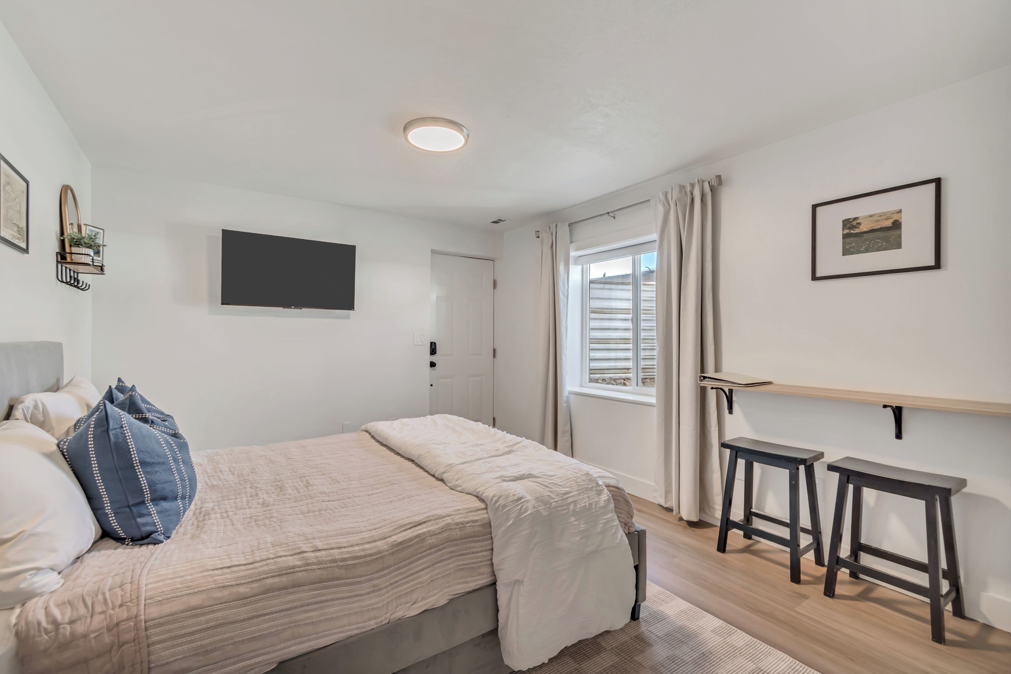 Une chambre à coucher avec un lit, une télévision, une fenêtre avec des rideaux et un petit tabouret.