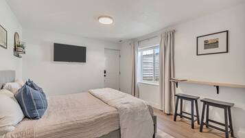 Une chambre à coucher avec un lit, une télévision, une fenêtre avec des rideaux et un petit tabouret.