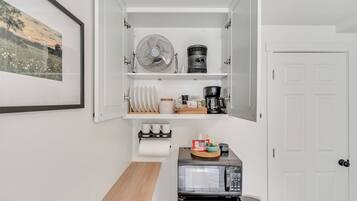 Une petite cuisine équipée d’un four à micro-ondes, d’une machine à café, d’un ventilateur et d’un tableau encadré au mur.