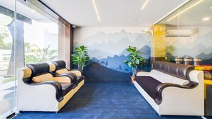 A hotel lobby with a blue carpet, two sofas with brown and beige cushions, a wall mural of mountains, and potted plants.