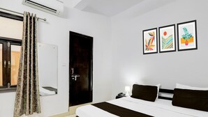 A hotel room with a bed, a nightstand, a phone, a wall-mounted air conditioner, a door, and three framed artworks. - Super Hotel O Indira Nagar (Lucknow)
