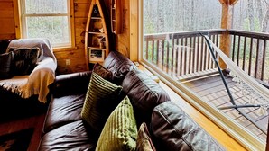 L’intérieur d’un chalet en bois est aménagé avec un canapé en cuir, une bibliothèque et une grande fenêtre donnant sur une terrasse.