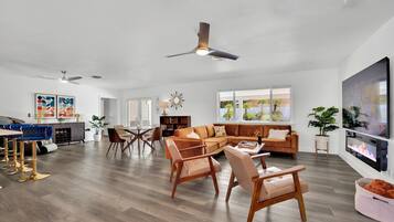 A spacious living room with a large sectional sofa, a dining area with a table and chairs, and a TV mounted on the wall.
