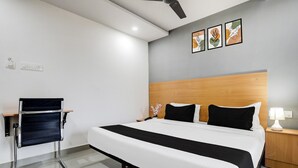 A modern hotel room with a large bed, a bedside table with a lamp, a wall-mounted power outlet, and a ceiling fan. - Premium Townhouse Shamshabad Near Airport (Hyderabad)