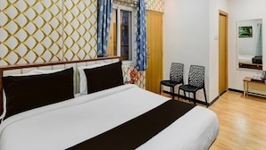 A hotel room with a bed, two chairs, a desk, and an air conditioning unit.