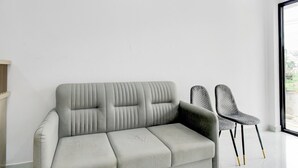 A modern living room with a grey sofa, two chairs, and a large window.