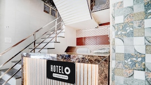 A hotel reception desk with a sign, a staircase, and a patterned wall. - Deluxe Krishna Janam Bhoomi (Mathura)