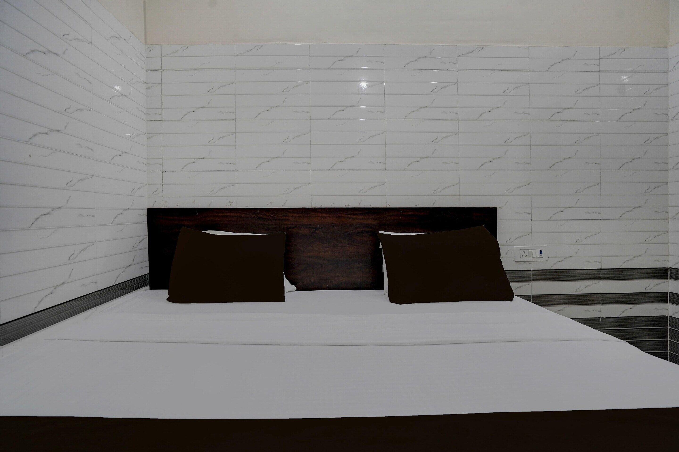 A hotel room with a bed, two pillows, a headboard, and tiled walls.