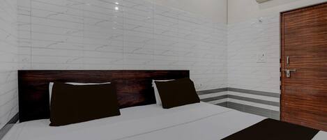 A hotel room with a large bed, a wooden headboard, white tiled walls, a wooden door, and an air conditioning unit.