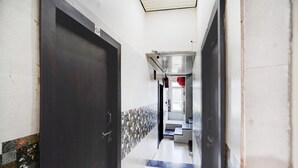 A hallway with a dark door, tiled walls, and a staircase leading to an upper level. - Deluxe Krishna Janam Bhoomi (Mathura)