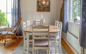 A dining room with a round table, white chairs, a painting above the table, and a window with curtains.
