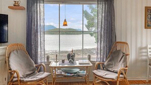 Una stanza con due poltrone in vimini, un tavolino con quotidiani, un vaso decorativo e vista su un lago e le montagne.