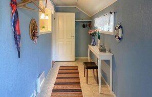 A hallway with a white door, a bench, a patterned rug, a small table with a vase, and a wall-mounted life preserver.