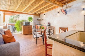A spacious outdoor kitchen area with wooden flooring, a dining table with chairs, a built-in stove, and a television.