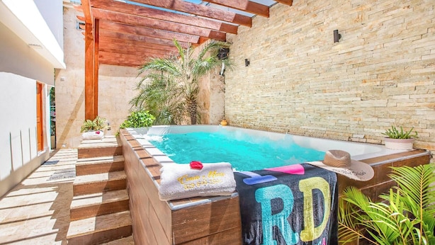 Un espace piscine aménagé sur le toit, avec une pergola en bois, un mur en briques et un petit palmier.