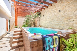 Ein Poolbereich auf dem Dach mit einer Holz-Pergola, einer Ziegelwand und einer kleinen Palme.