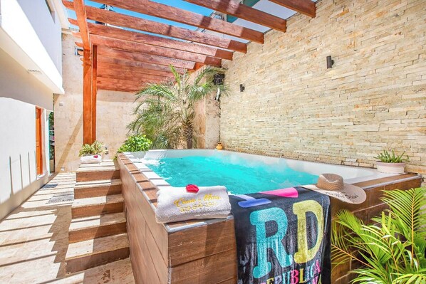 A rooftop pool area with a wooden pergola, a brick wall, and a small palm tree.