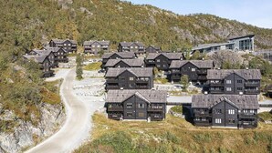 Un conjunto de cabañas de madera con un camino de tierra que las lleva, rodeado de un paisaje montañoso.