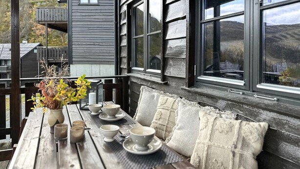 Una terraza de madera con una mesa dispuesta para comer, un banco y vistas al campo.