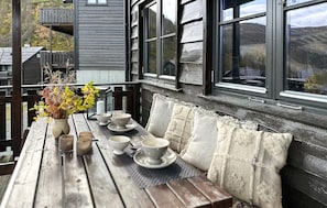 A wooden deck with a table set for dining, a bench, and a view of the countryside.