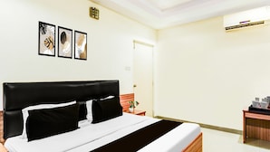 Een hotelkamer met een bed, een nachtkastje, een klein tafeltje met een plant en kunstwerken in een lijst aan de muur.