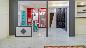 Un hall d’hôtel doté d’un sol en marbre, d’un comptoir d’accueil et d’un espace repas avec des chaises et des tables.