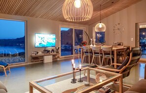 A modern living room with a large TV, dining area, and a view of the sea. - Lovely home in Farsund (Farsund)