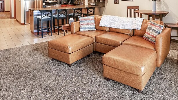 A spacious living area with a large L-shaped sectional sofa, a kitchen with modern appliances, and a dining area with a small table and chairs.