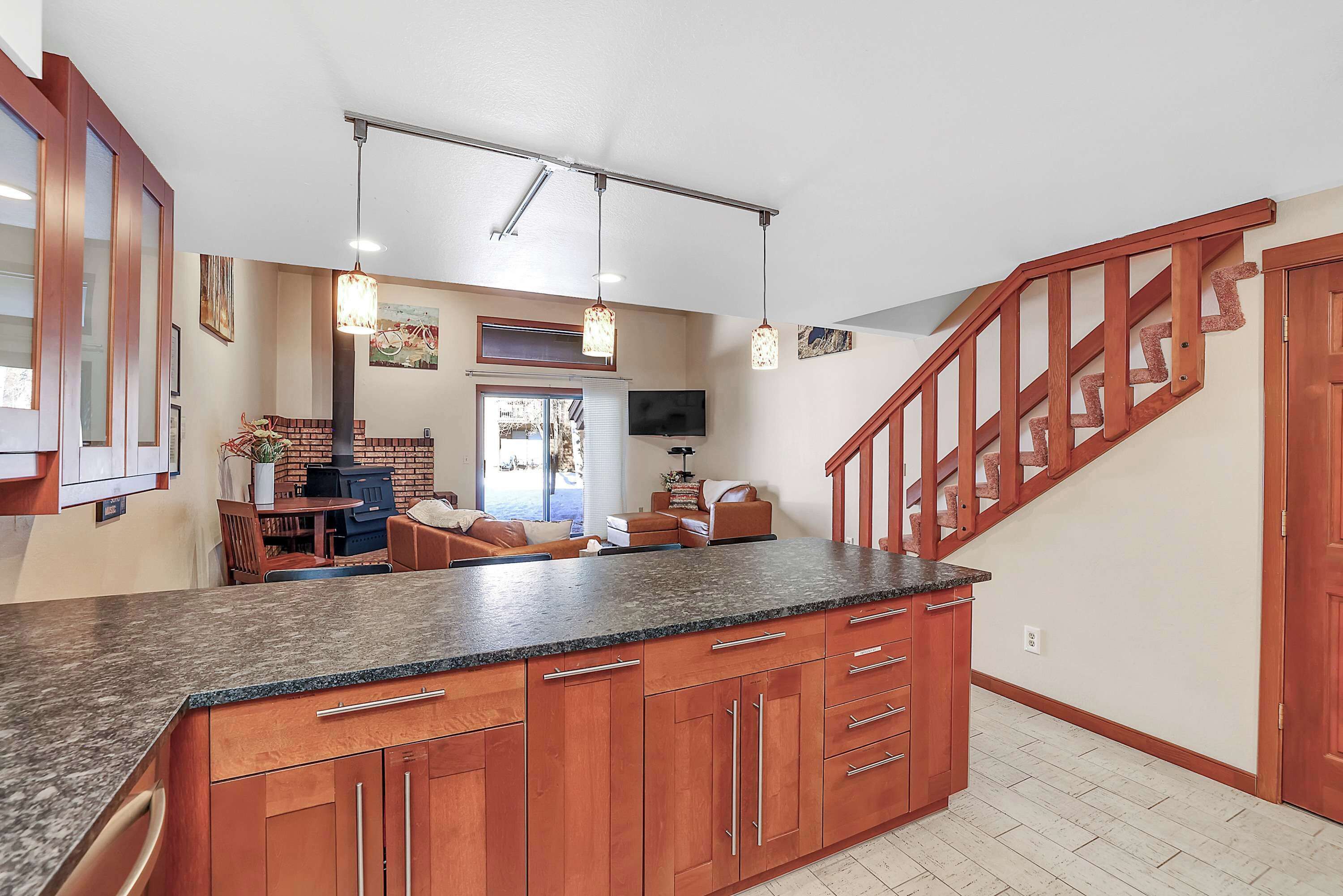 Une cuisine dotée de plans de travail en granit, d’armoires en bois et d’un escalier en bois.