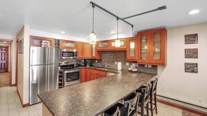 A modern kitchen with granite countertops, stainless steel appliances, wooden cabinets, and pendant lighting.
