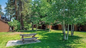 A wooden cabin with a picnic table in a grassy yard surrounded by trees.