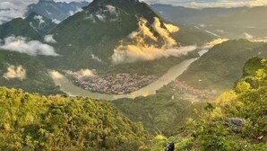 Eine gebirgige Landschaft mit einem Fluss, einer Brücke und einer Stadt.